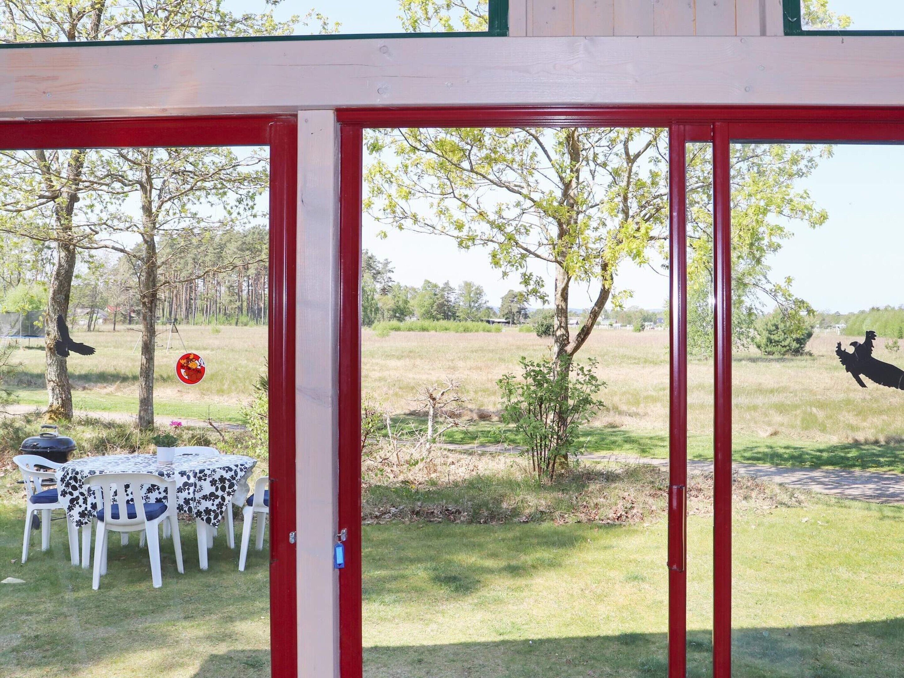 An outdoor seating area with a table and chairs, a red structure, and a view of a field with trees and a statue.