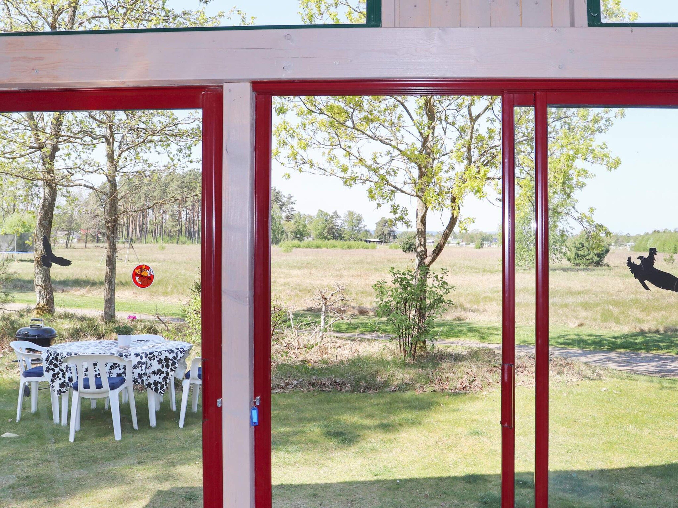 An outdoor seating area with a table and chairs, a red structure, and a view of a field with trees and a statue.