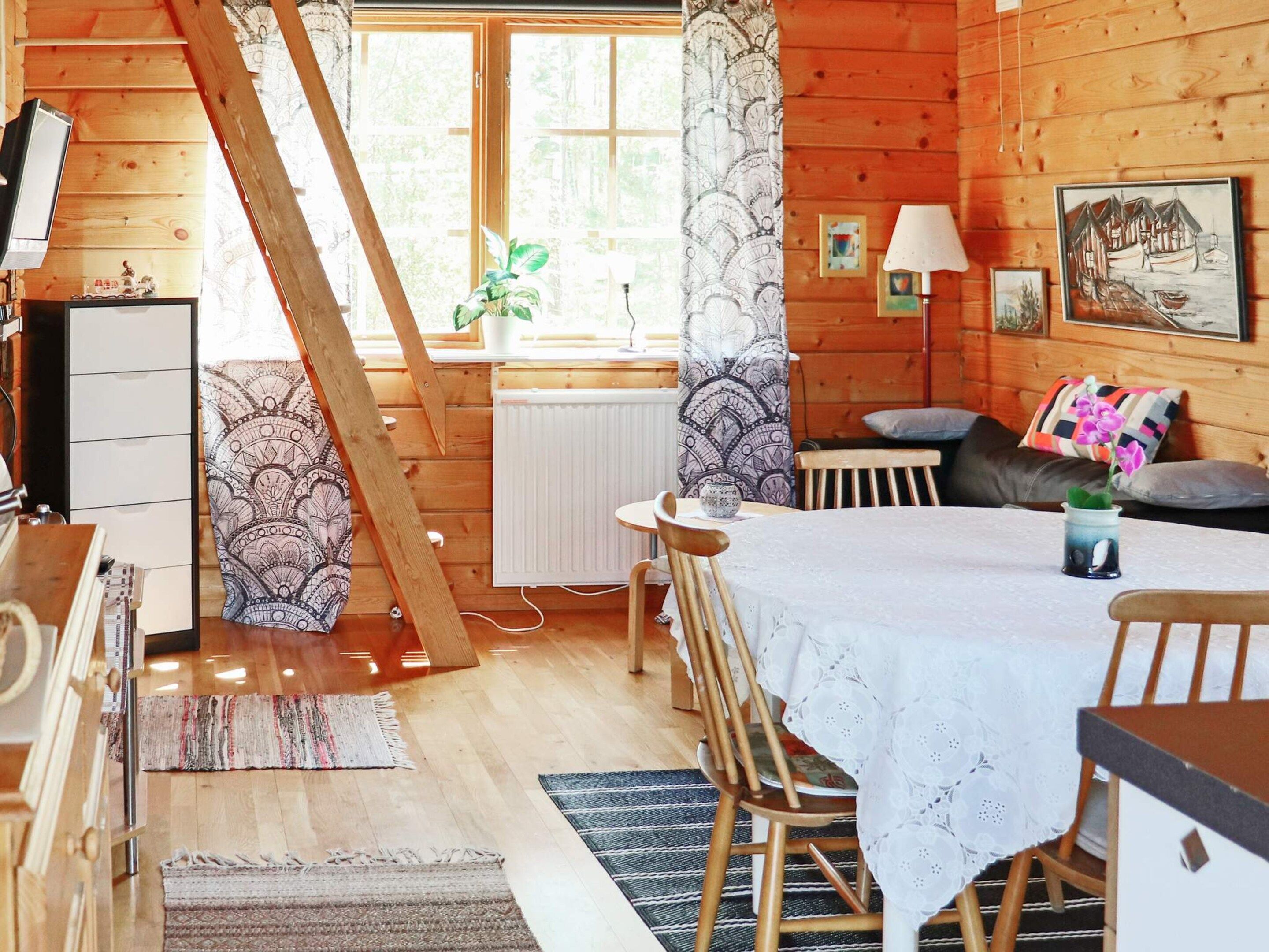 A cozy cabin interior with a dining area, a sofa, and a window with curtains.