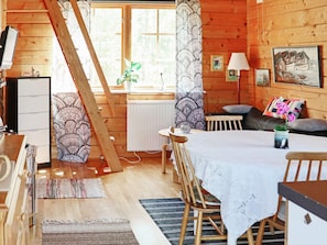 A cozy cabin interior with a dining area, a sofa, and a window with curtains.