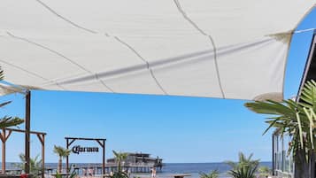 A beachside patio with wooden furniture, a white canopy, and a view of the sea.