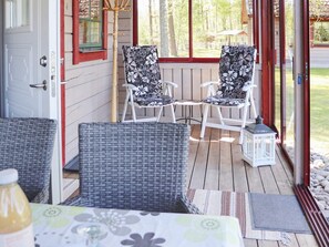 A covered outdoor seating area with wicker chairs and a table, a wooden deck, and a view of the surrounding trees.