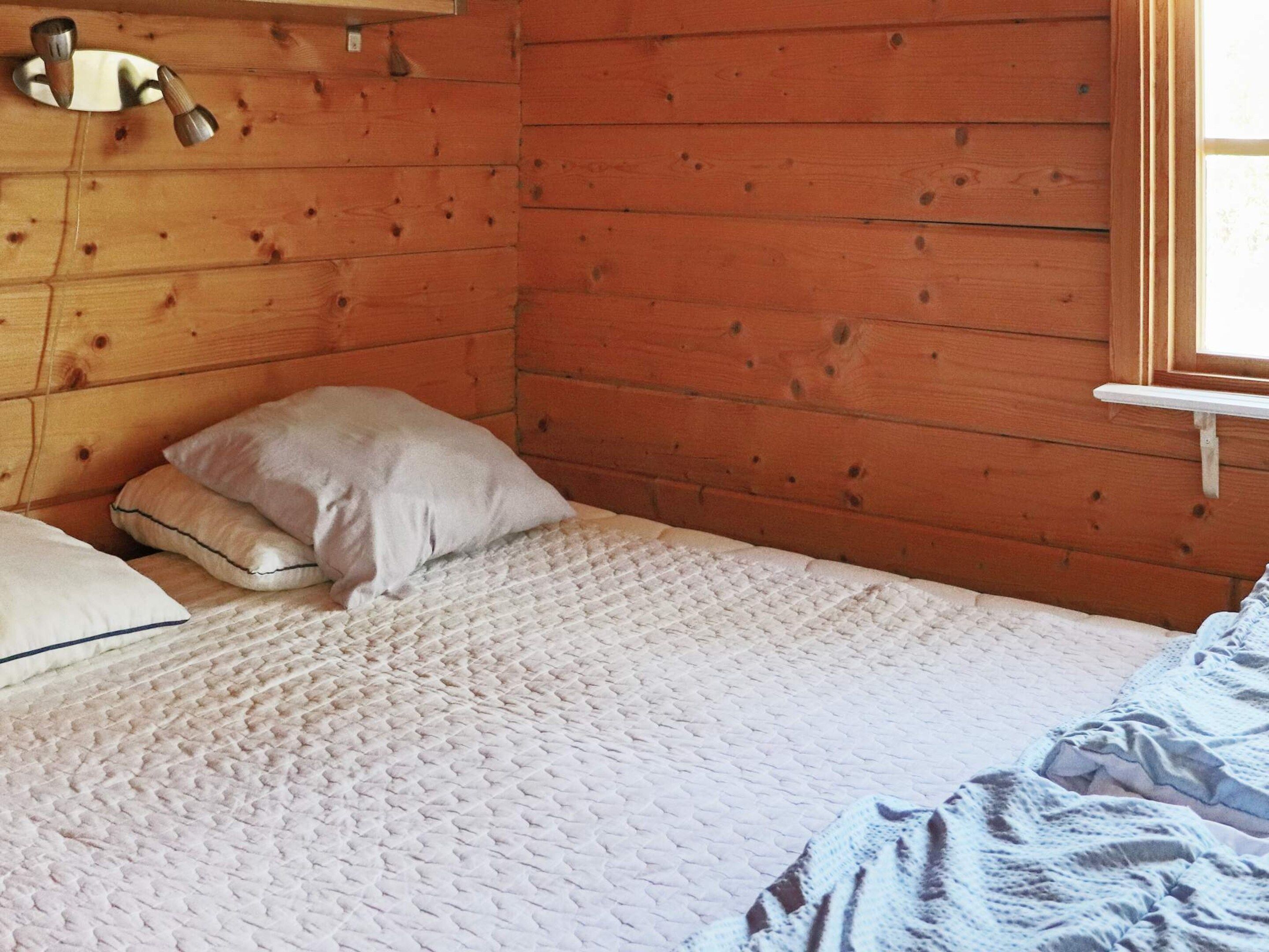 A wooden room with a bed, pillows, and a window.