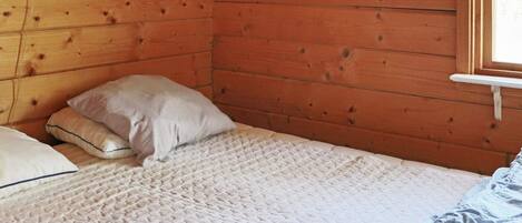 Una stanza in legno con un letto, dei cuscini e una finestra.