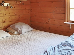 A wooden room with a bed, pillows, and a window.