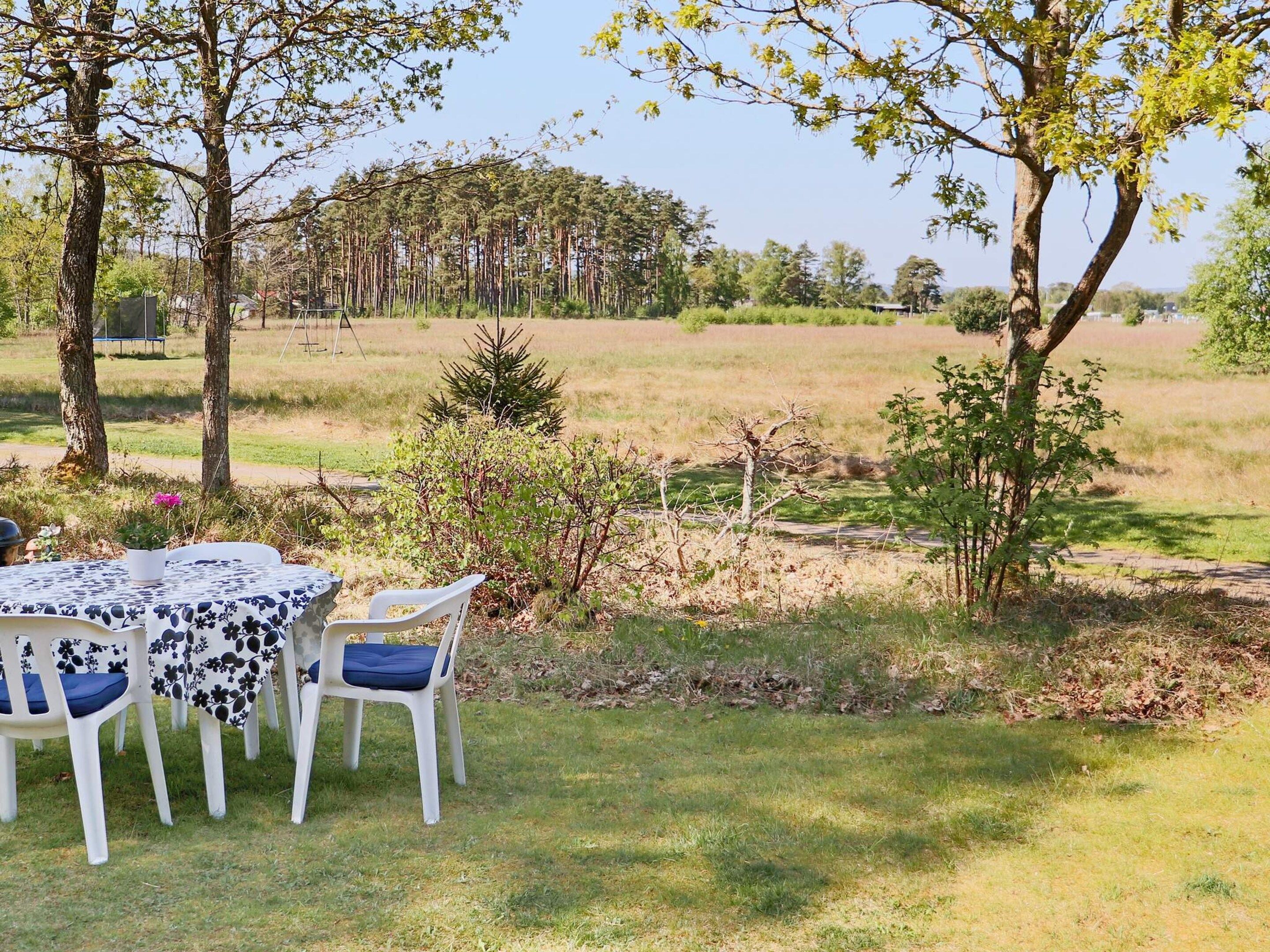 An outdoor dining area with a table and chairs, surrounded by trees and a grassy field.