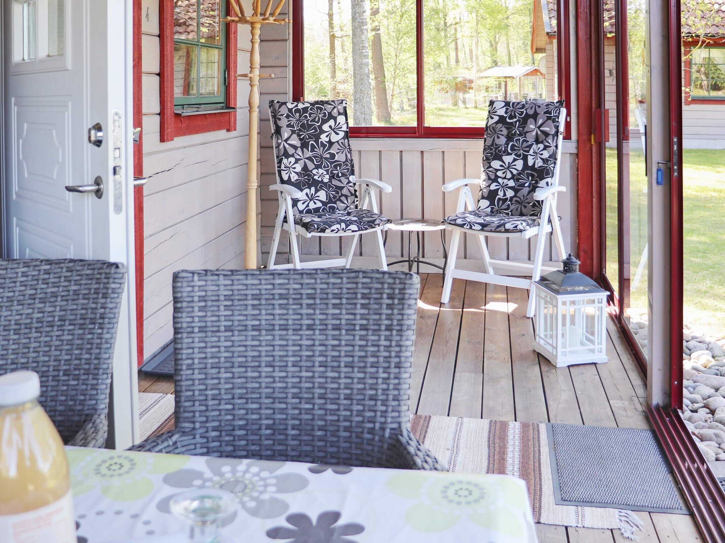 Un portico riparato con sedie in vimini e un tavolo, un patio in legno e vista sugli alberi circostanti.