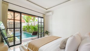 Quarto com uma cama grande, vista para uma piscina e porta de correr para uma área externa com plantas.