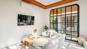 Sala de estar moderna com teto de madeira, uma janela grande com moldura preta, sofá branco, mesa de centro de madeira e TV fixada na parede.
