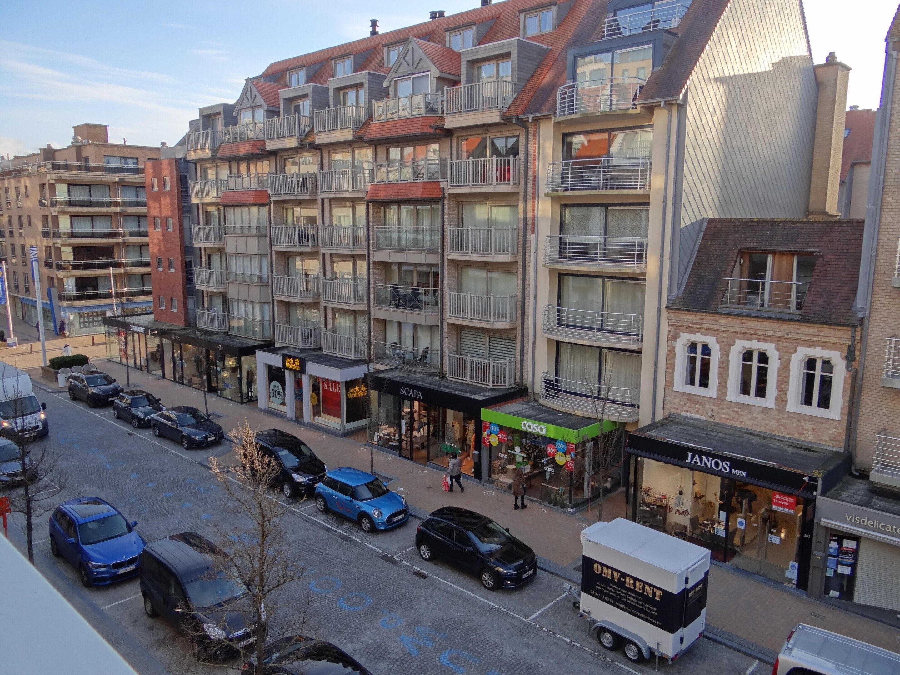 A multi-story building with balconies, storefronts, and parked cars.