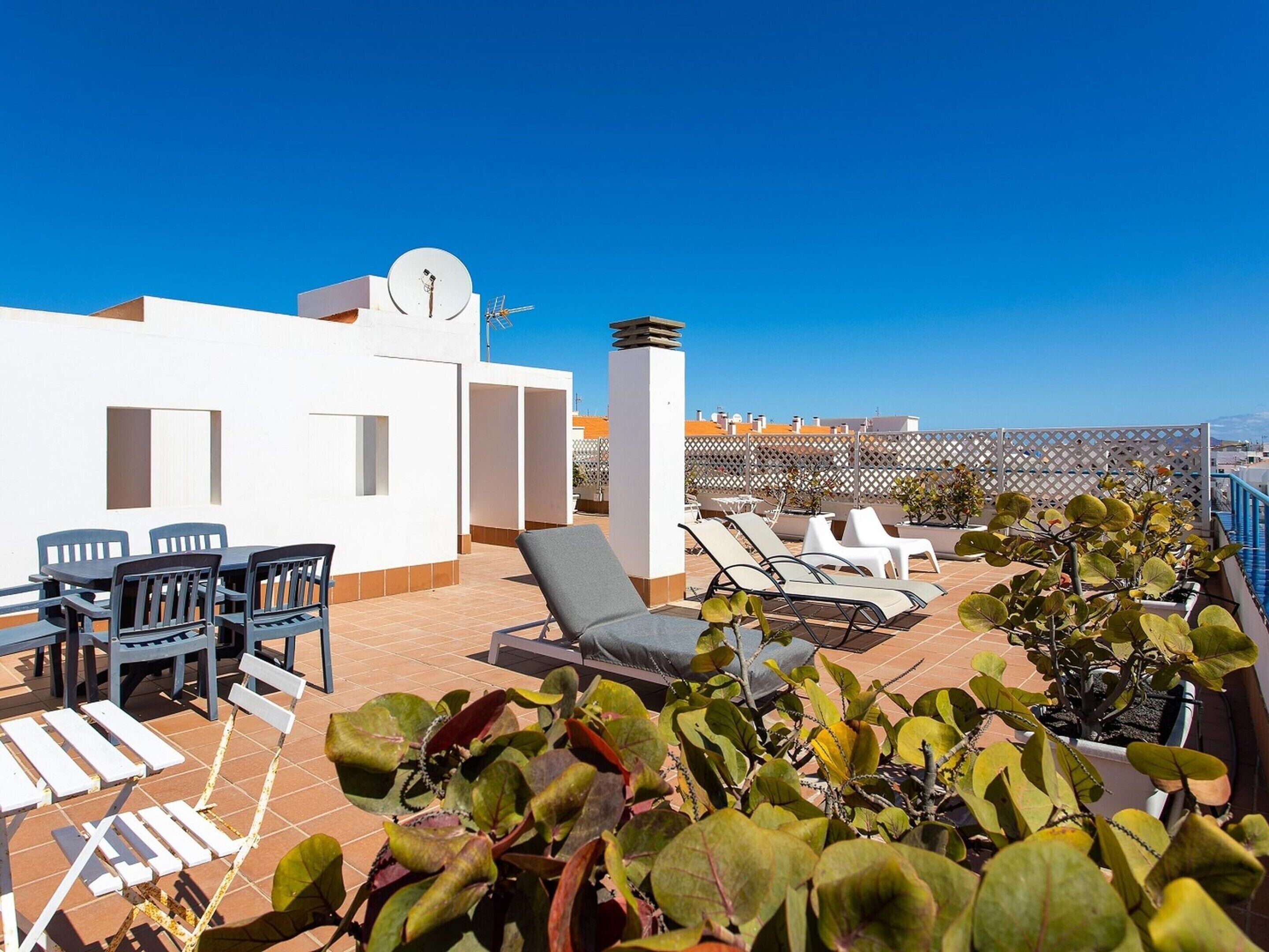 A rooftop terrace with outdoor seating, a satellite dish, and potted plants.