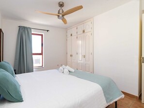 A bedroom with a bed, a ceiling fan, a window with curtains, and a wardrobe. - Belvilla by OYO Uptown I (La Oliva)
