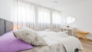 Ein Schlafzimmer mit Bett, Kissen, einem Nachttisch, einem Spiegel und einem Fenster mit Vorhängen.
