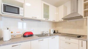 Eine moderne Küche mit weißen Schränken, einer Mikrowelle, einem Toaster und einer Spüle aus Edelstahl.
