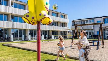 Ein Spielplatz mit einer gelben Kletterkonstruktion, einem Volleyballnetz und einer Schaukel.
