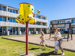 A playground with a yellow climbing structure, a volleyball net, and a swing set. - 4 Person Holiday Home on a Holiday Park in Blokhus (Blokhus)