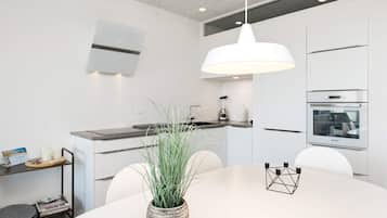 Une cuisine moderne avec des meubles blancs, un îlot central, un four encastré et un luminaire suspendu.