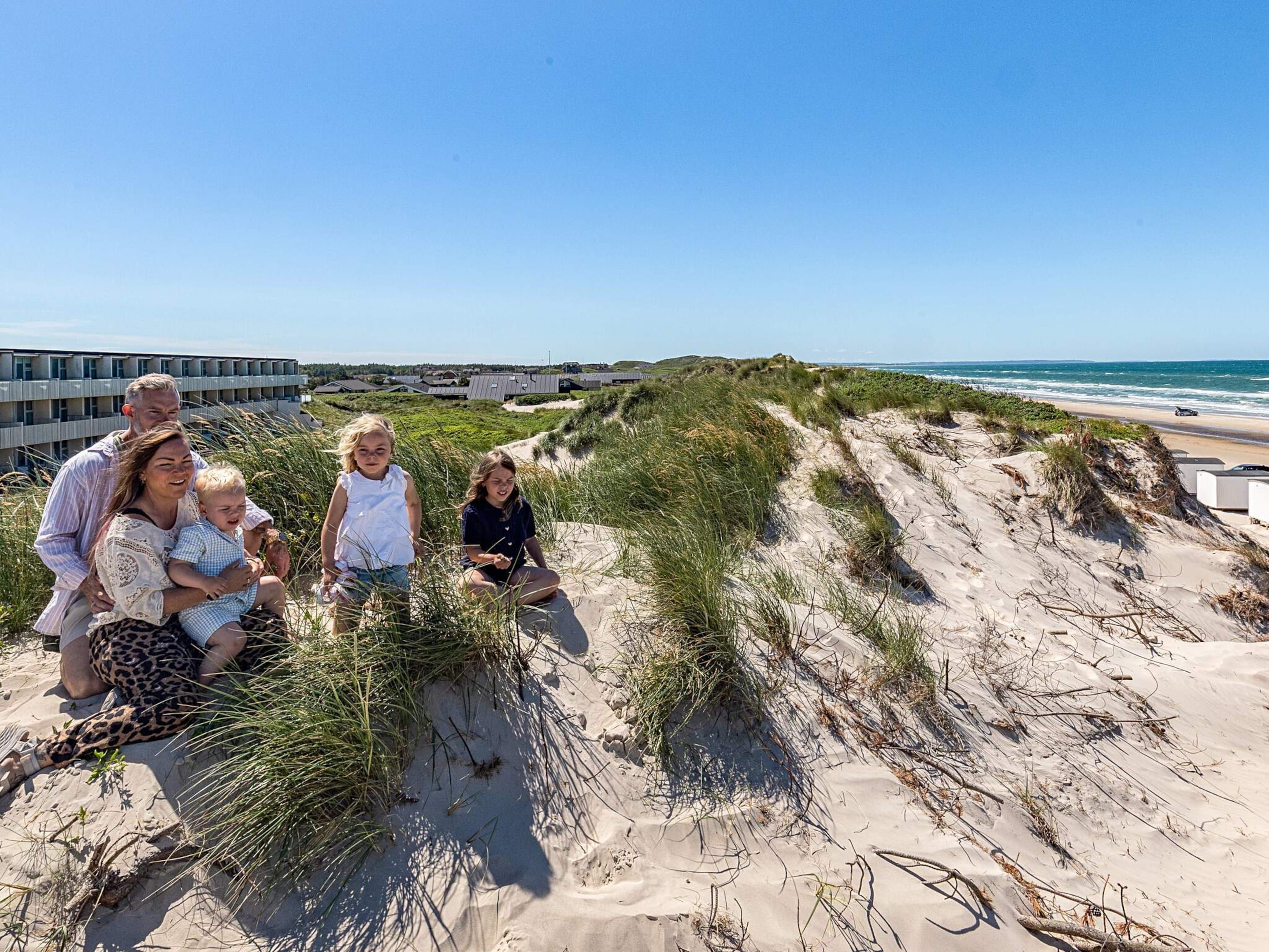A family on a sandy beach with dunes and a building in the background.