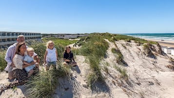 A family on a sandy beach with dunes and a building in the background.