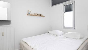 A bedroom with a bed, a radiator, a window with blinds, and a wall-mounted shelf with the word "LOVE".