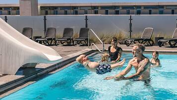 A swimming pool with a slide, lounge chairs, and a building in the background.