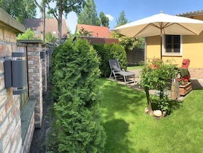 A backyard with a well-maintained lawn, a tall coniferous tree, a patio chair, and a large umbrella. - Pleasant Apartment in Schwielowsee (Schwielowsee)