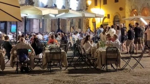 An outdoor dining area with tables and chairs, set against a historic building facade with multiple windows and arches.