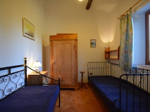 A bedroom with two beds, a wooden door, a small table with a lamp, and a window with a curtain.