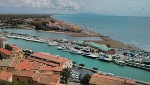 A coastal town with a marina, buildings with red-tiled roofs, and a clear view of the sea.