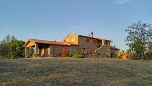 A stone house with a red-tiled roof, a covered porch, and a large grassy yard.