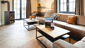 Una sala de estar moderna con un sofá, dos mesas de centro, una chimenea y ventanas grandes con cortinas.