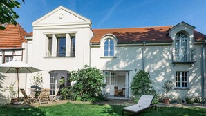 A white two-story house with a red-tiled roof, a covered patio with outdoor furniture, and a lawn. - Holiday Apartment Remise - Ground Floor (Werder (Havel))
