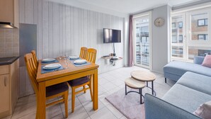 Um apartamento moderno com área de jantar, televisão na parede, sofá e janela com vista para edifícios.