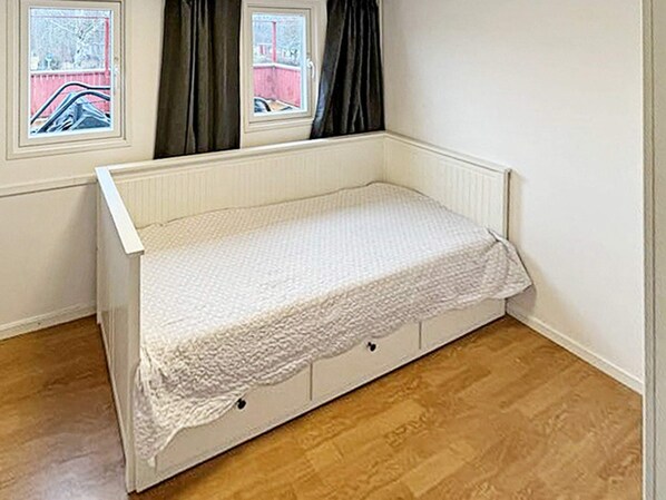 A small, single-bed room with a white bed, a window with curtains, and a wooden floor. - 4 Person Holiday Home in Sodertalje (Sodertalje)
