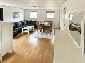 A room with a wooden floor, a black leather sofa, a white coffee table, a dining table with chairs, and a large mirror. - 4 Person Holiday Home in Sodertalje (Sodertalje)
