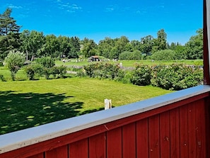 A red wooden balcony overlooking a green field with trees and a small building in the distance. - 4 Person Holiday Home in Sodertalje (Sodertalje)