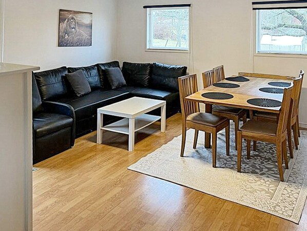 A living room with a black leather sofa, a white coffee table, a wooden dining table with chairs, and a patterned rug.