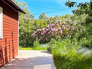 A red wooden building with a pathway leading to a garden with pink flowers. - 4 Person Holiday Home in Sodertalje (Sodertalje)