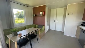 Cocina compacta con una mesa de comedor, sillas, un refrigerador pequeño y una ventana con vista a follaje.