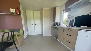 Cocina compacta con lavavajillas, cafetera y microondas. Zona de comedor con una silla y una mesa.