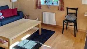 Una habitación acogedora con una mesa de madera, un sofá azul con cojines rojos, una silla negra y una ventana con cortinas.