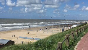 A beach with a sandy shore, a grassy area with a fence, and a view of the ocean with people and kites. - Lively Apartment in Norderney (Norderney)