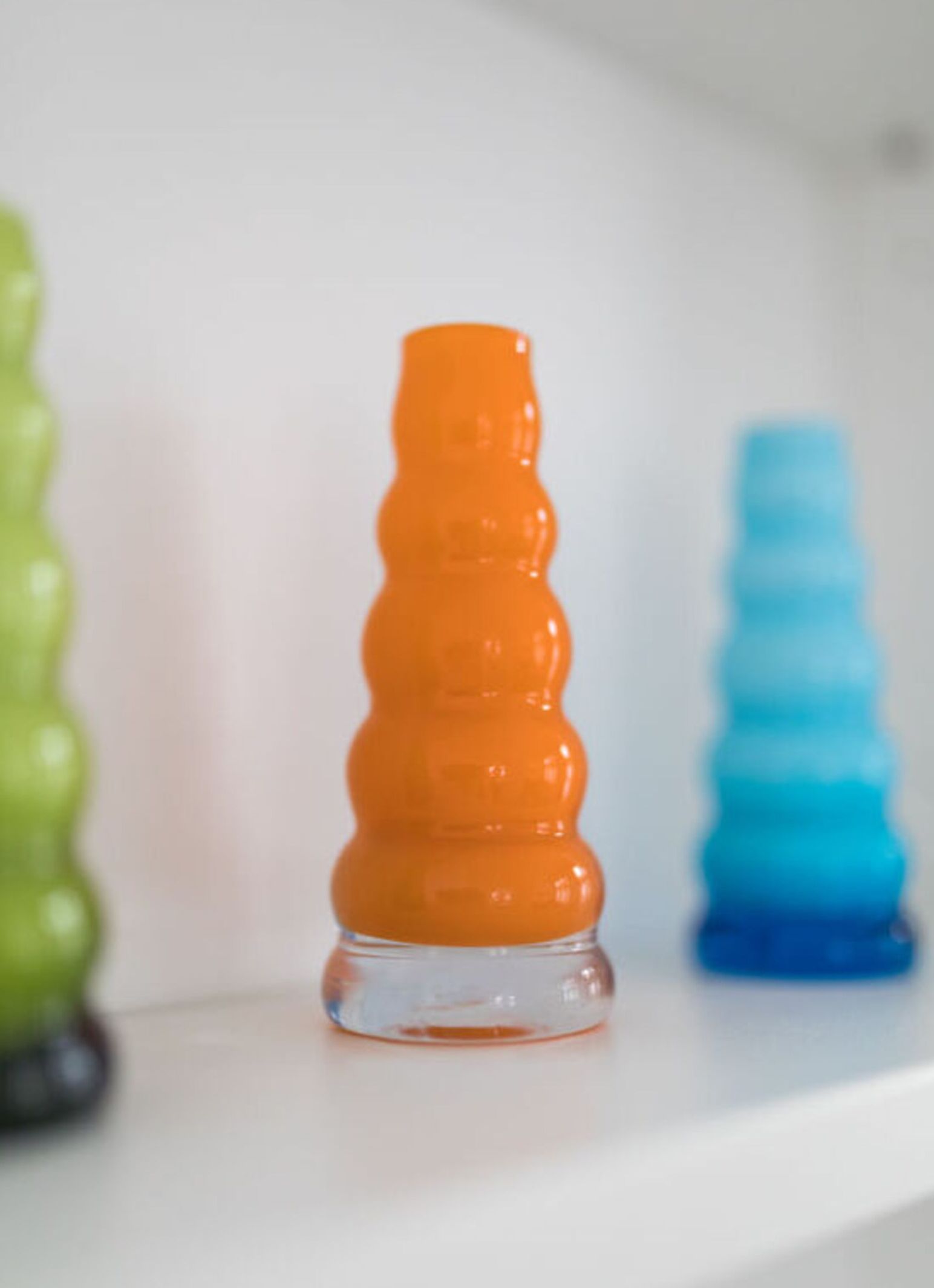 Een glazen fles met een golvend, deelbaar ontwerp, geplaatst op een wit oppervlak.