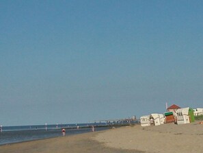 A beach with a row of numbered beach huts and a pier in the background. - Red Sand Modern Retreat (Wangerland)