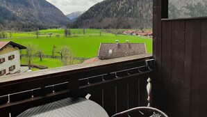 A view from a balcony overlooking a green valley with mountains in the background. - Ferienwohnung in Bayrischzell (Bayrischzell)