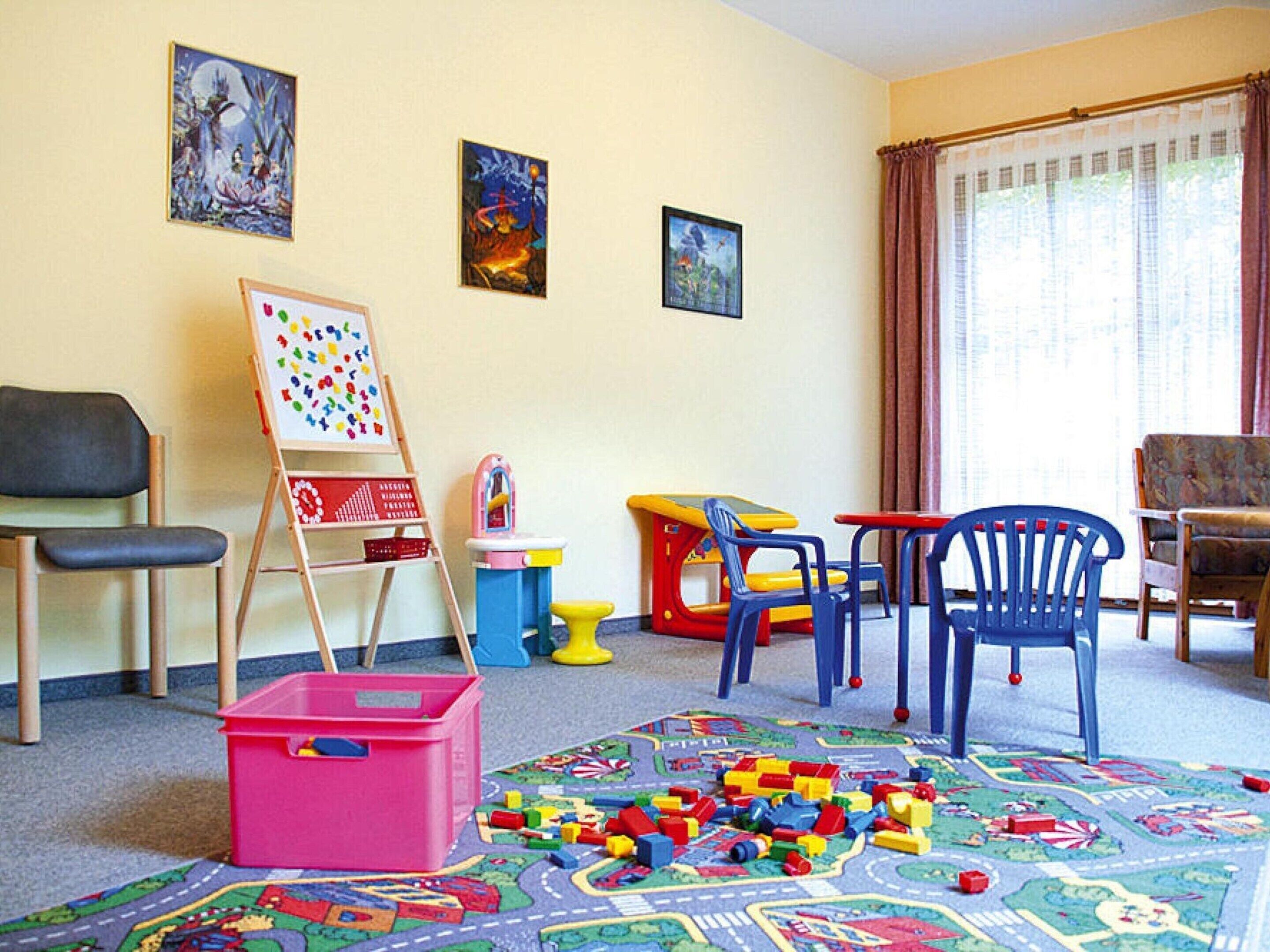 Un cuarto de juegos para niños con un tapete de colores, una pizarra y varios juguetes esparcidos por el suelo.
