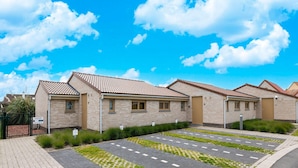 Uma fileira de casas modernas de tijolo com telhados de cerâmica, um caminho de entrada pavimentado com áreas de grama e um céu azul claro.