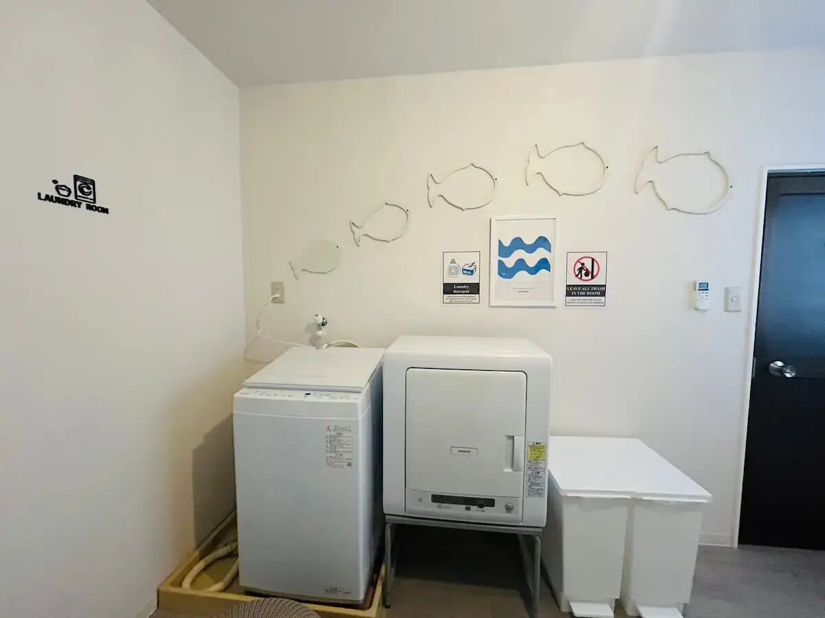 Een wasserette met twee wasmachines en een droogrek. Borden aan de muur geven de functie van de ruimte en veiligheidsinstructies aan.