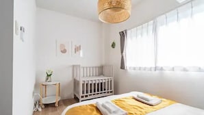 A modern bedroom with a crib, a bedside table with a plant, and a large bed with a yellow blanket. - Wagyu House (Osaka)