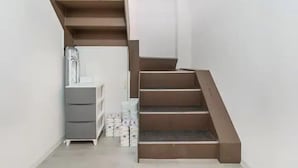 A narrow stairway with a wooden handrail and steps, leading to a landing with a white wall and a grey storage unit. - Wagyu House (Osaka)